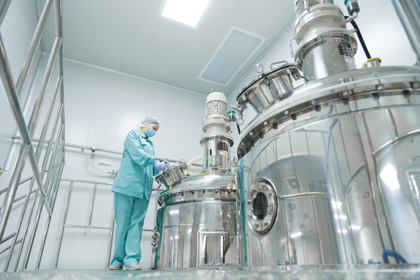 Pharmaceutical factory woman worker in protective clothing operating production line in sterile environment